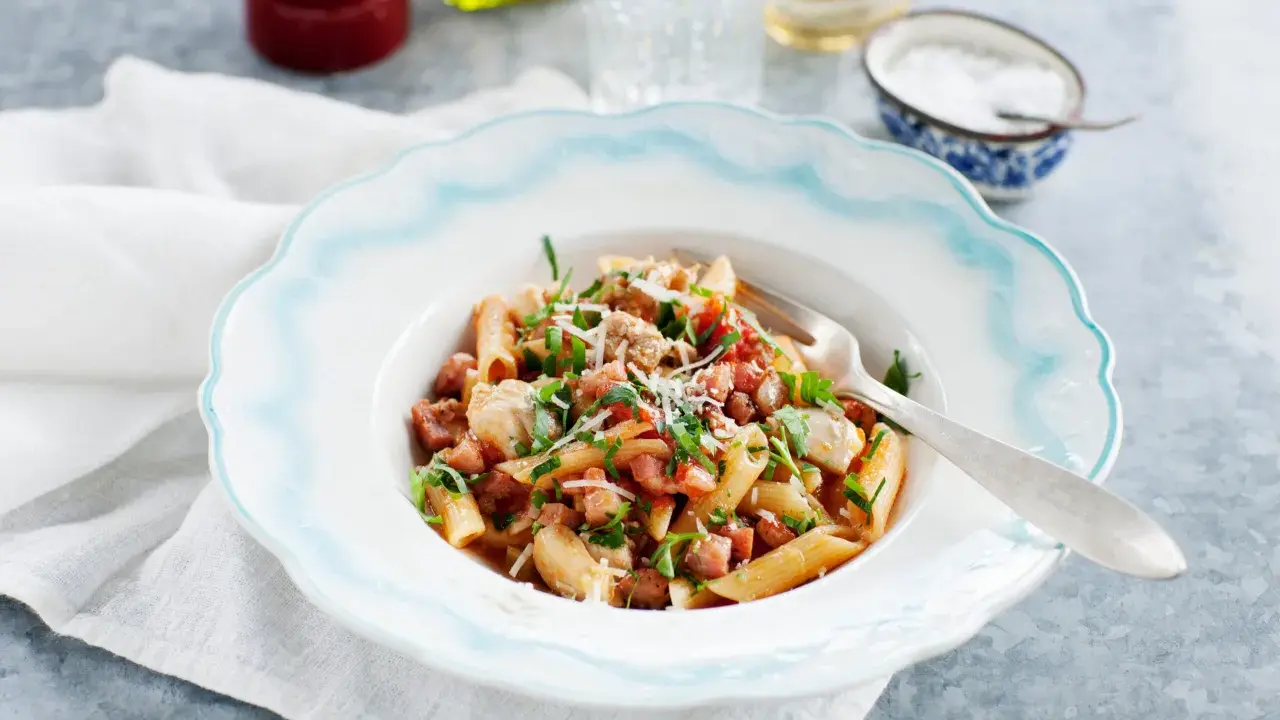 En tallrik med penne pasta, kyckling och tärnad pancetta, toppad med persilja och parmesan. Ett enkelt pancetta recept för en god middag.