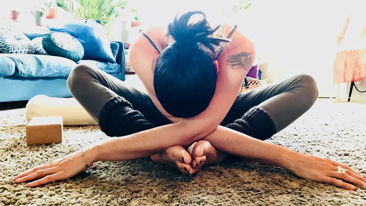 En kvinna i en djup yogaställning på en fluffig matta, omfamnar sig själv i en gest av nonduality.