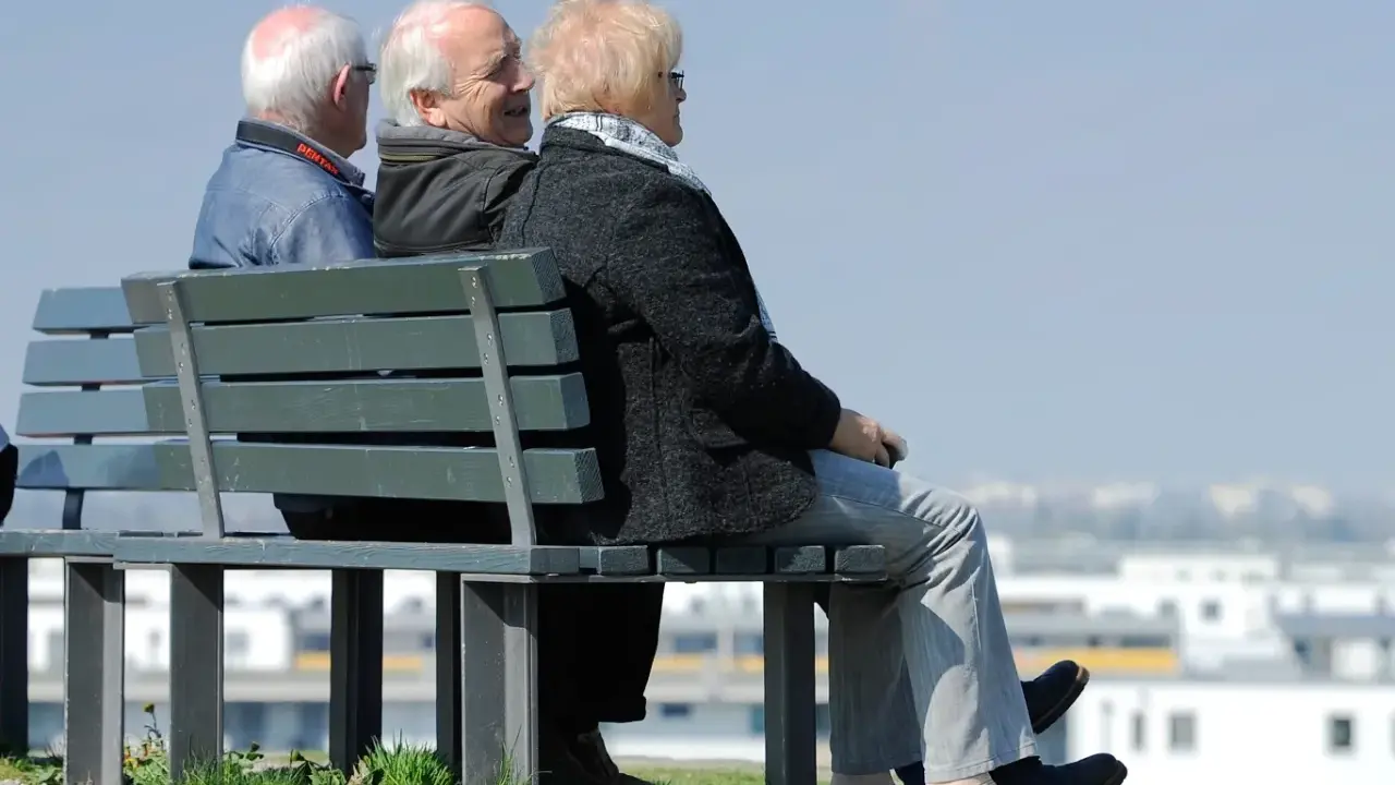 Trzech seniorów siedzi na ławce, rozmawiając. Może to dyskusja o tym, czym jest emerytura pomostowa i jakie daje możliwości.