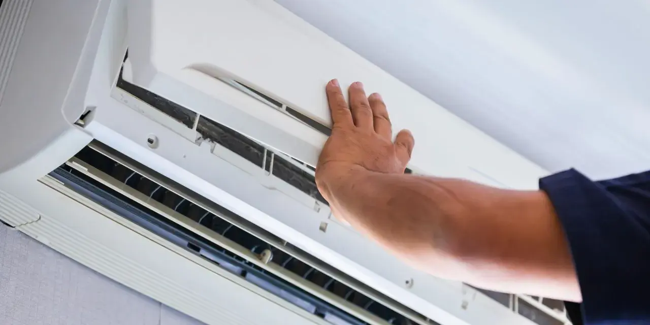 Main d'un technicien ouvrant un climatiseur pour vérifier l'eau et le filtre.