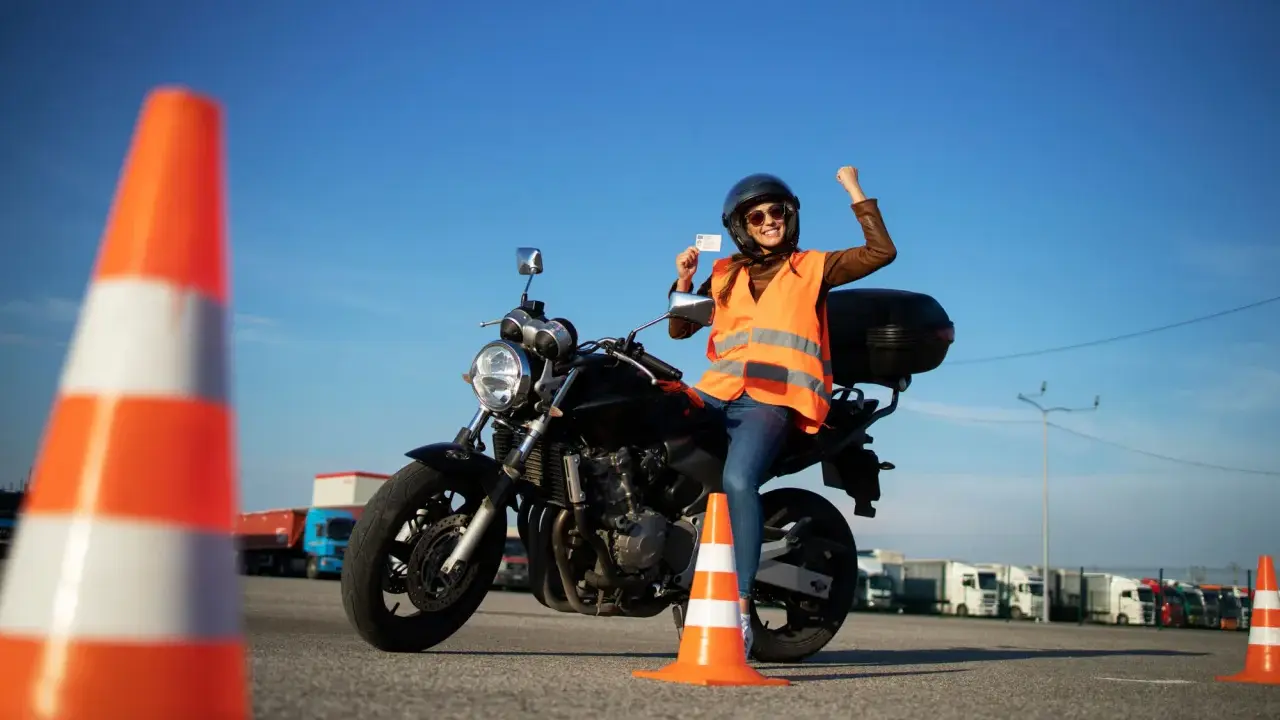 Szczęśliwa motocyklistka z prawem jazdy kategorii A3 w ręku, siedząca na motocyklu, świętuje sukces na placu manewrowym.