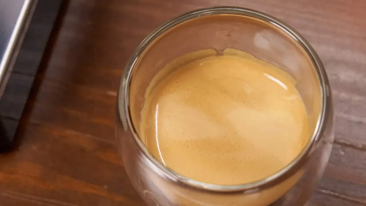 Ein Glas Espresso mit einer feinen Crema auf einem Holztisch. Ein kleiner Schuss Sahne macht den Kaffee mit Sahne gesund und lecker.