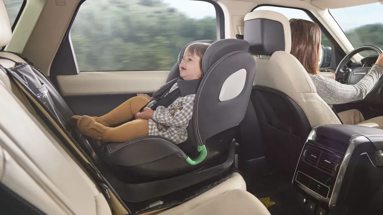 Bebé sonriente en silla de coche a contramarcha, viajando segura mientras mamá conduce.