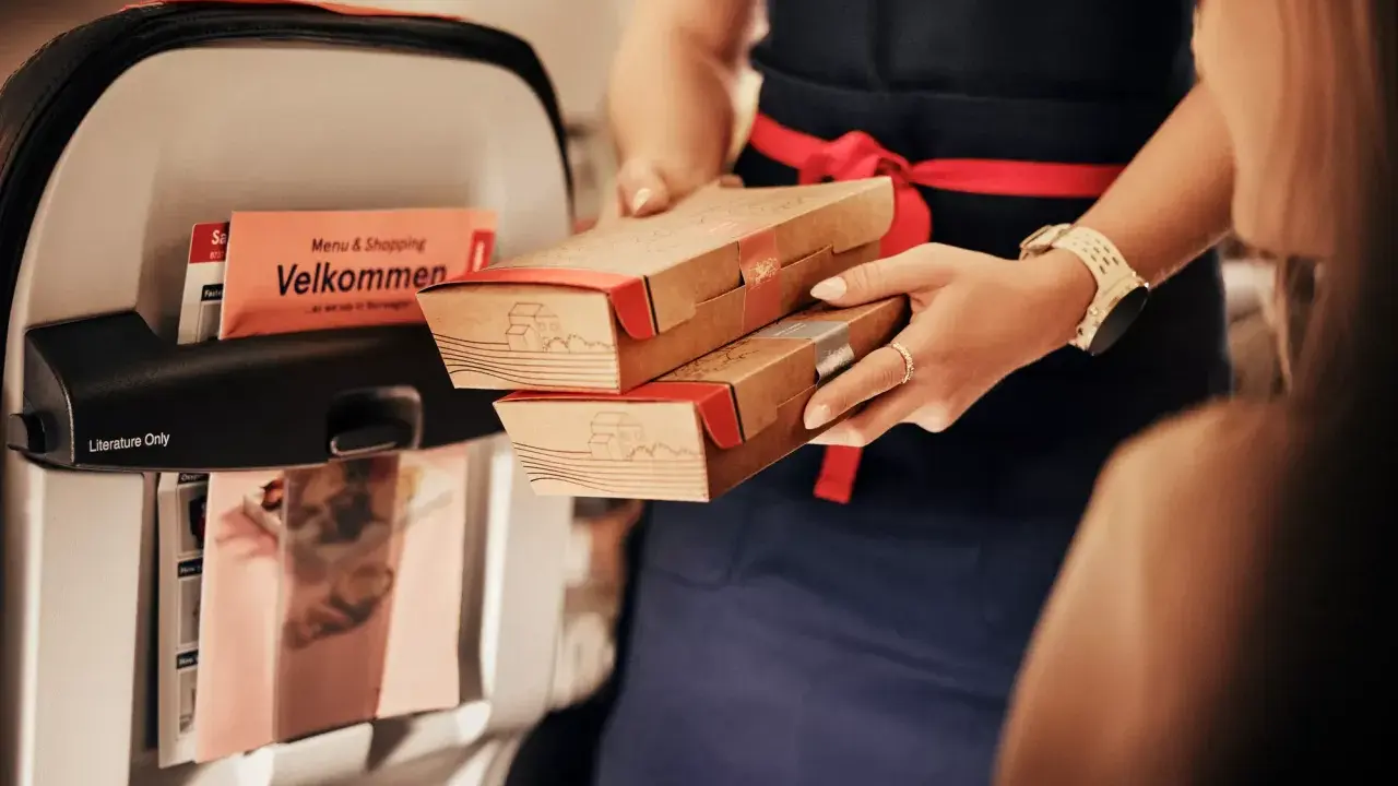 Serverar mat ombord, kanske en del av norwegian taxfree ombord-utbudet. En "Velkommen"-folder syns i fickan.