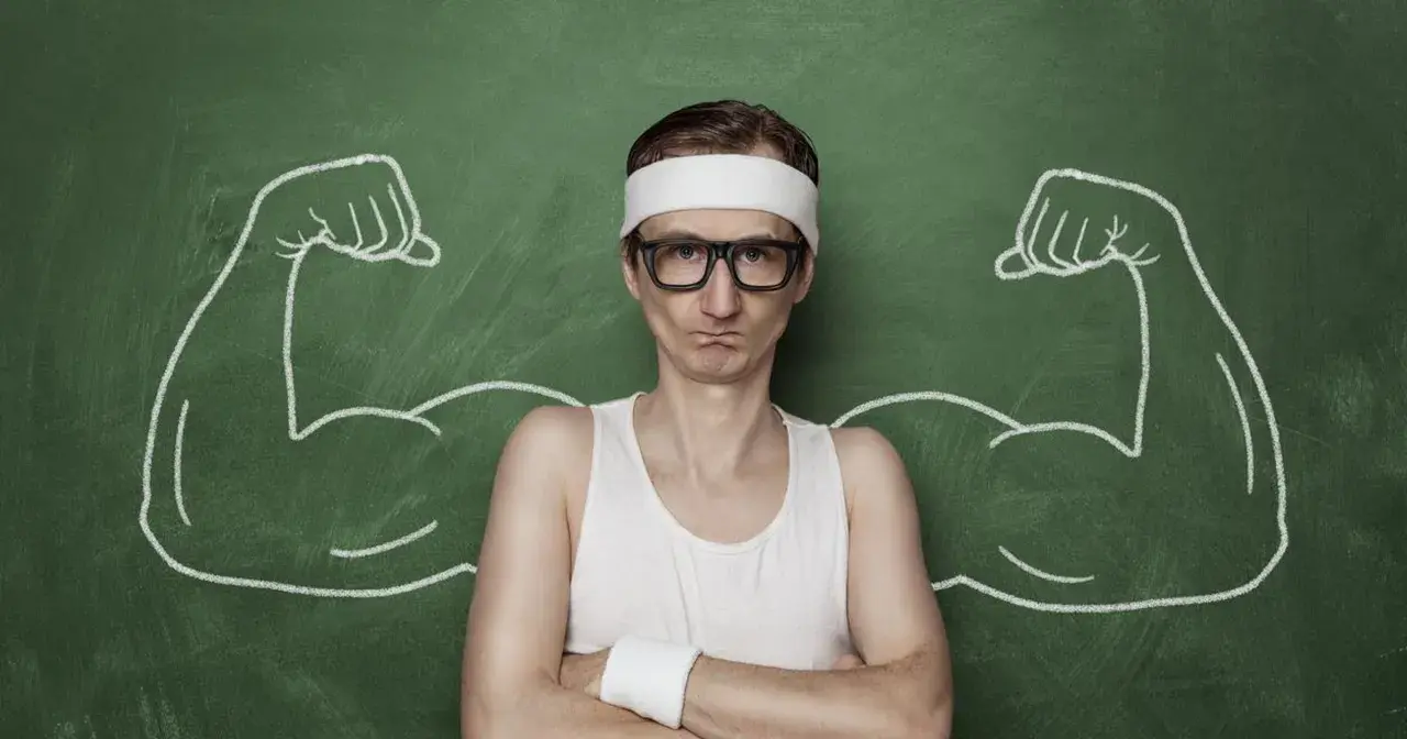Chudy mężczyzna w okularach i opasce na głowie, z narysowanymi po bokach bicepsami, jakby po zażyciu omnadren 250.
