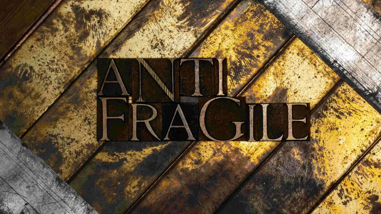 Lettere di metallo con la scritta "ANTI FRAGILE" su uno sfondo ruvido e dorato, simbolo di antifragilità e resilienza.