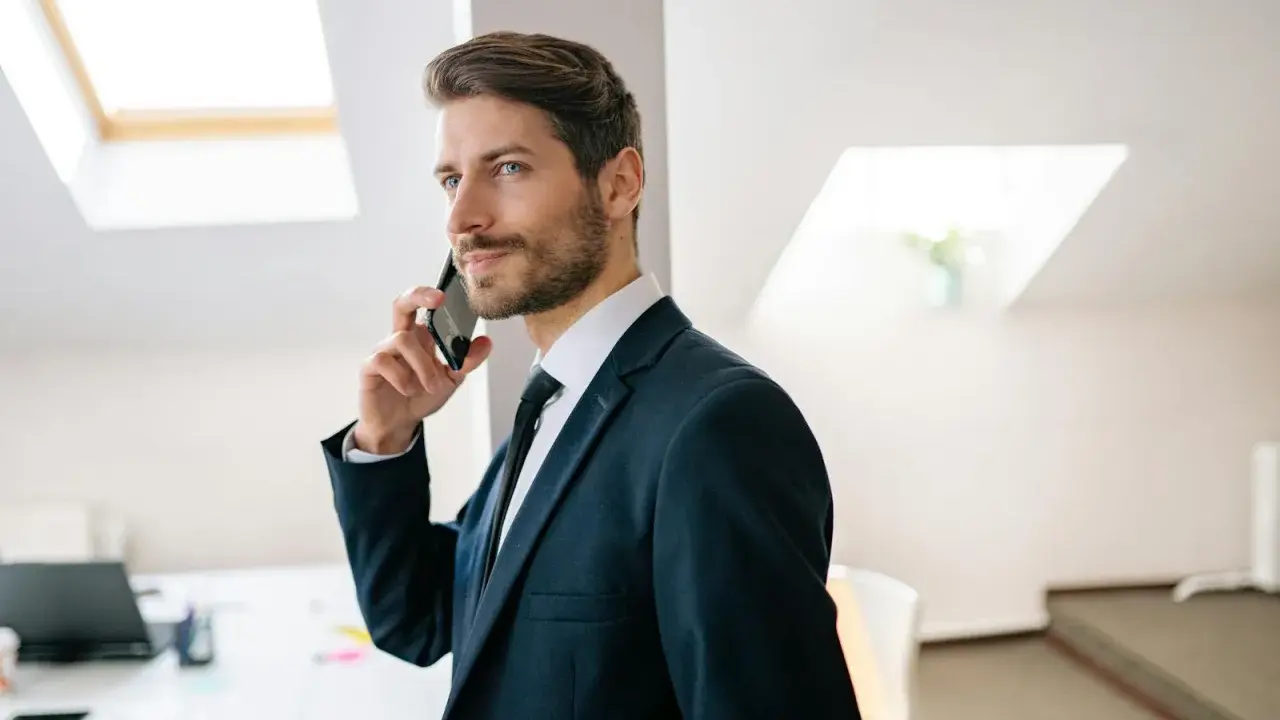 Mężczyzna w garniturze rozmawia przez telefon, jego wyraz twarzy sugeruje, że nastąpiła **zmiana głosu podczas rozmowy**.