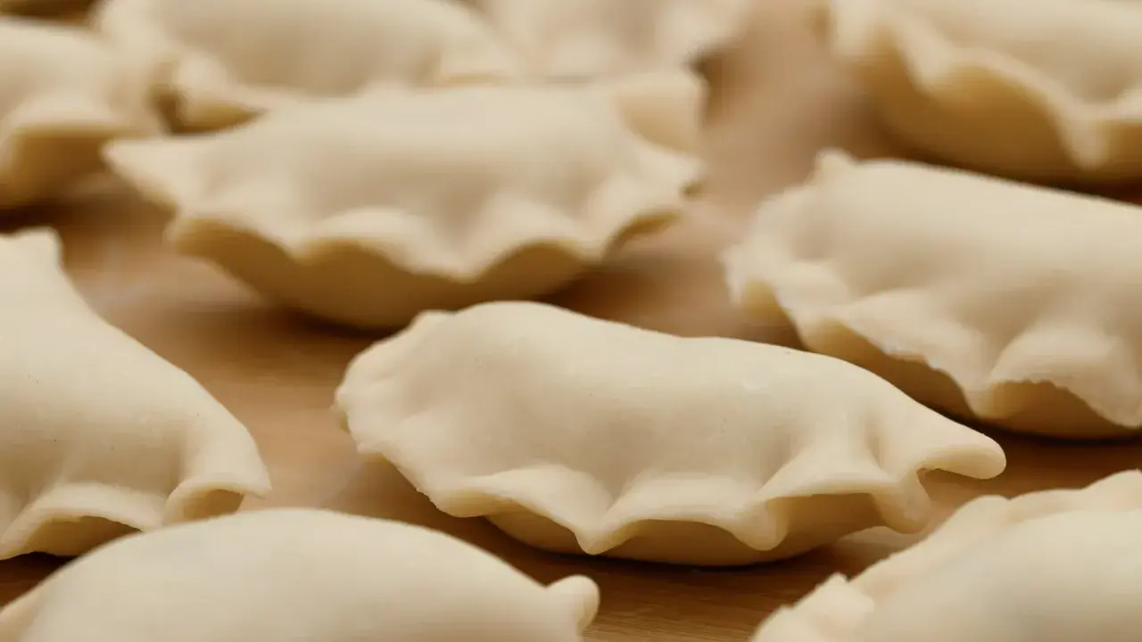 Surowe pierogi z jagodami leżą na drewnianej desce, gotowe do gotowania.