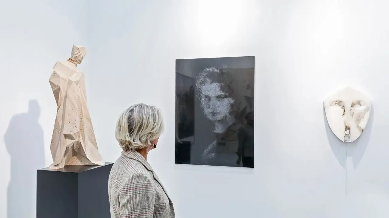 A woman views a collection of art, including a wooden sculpture and a portrait, appreciating art as an asset class.