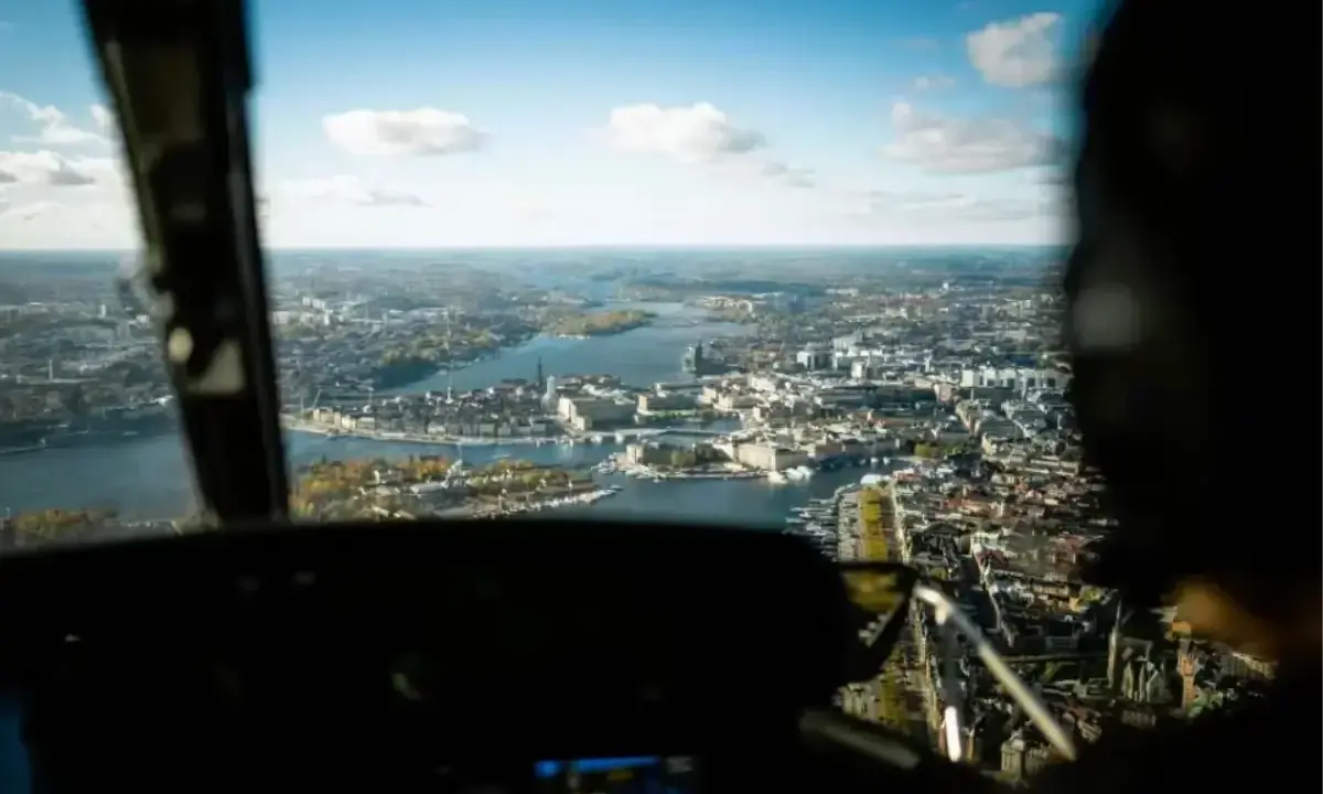 Vy från en helikopter över Stockholm. Staden breder ut sig vid vattnet under en klarblå himmel med moln.