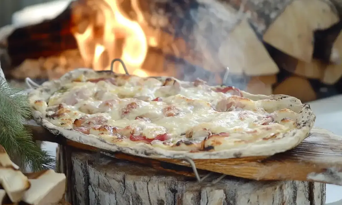 Flammekueche dorée et fumante, garnie de lardons et de fromage fondant, cuite au feu de bois.