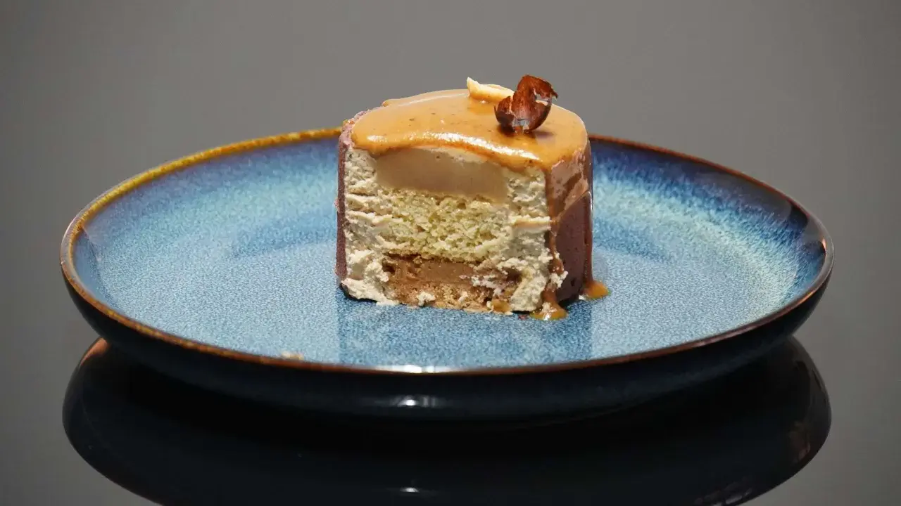Tranche d'entremet aux couches aériennes, surmontée d'un glaçage caramel et d'une noisette croquante. Le biscuit noisette pour entremet offre une texture légère et savoureuse.