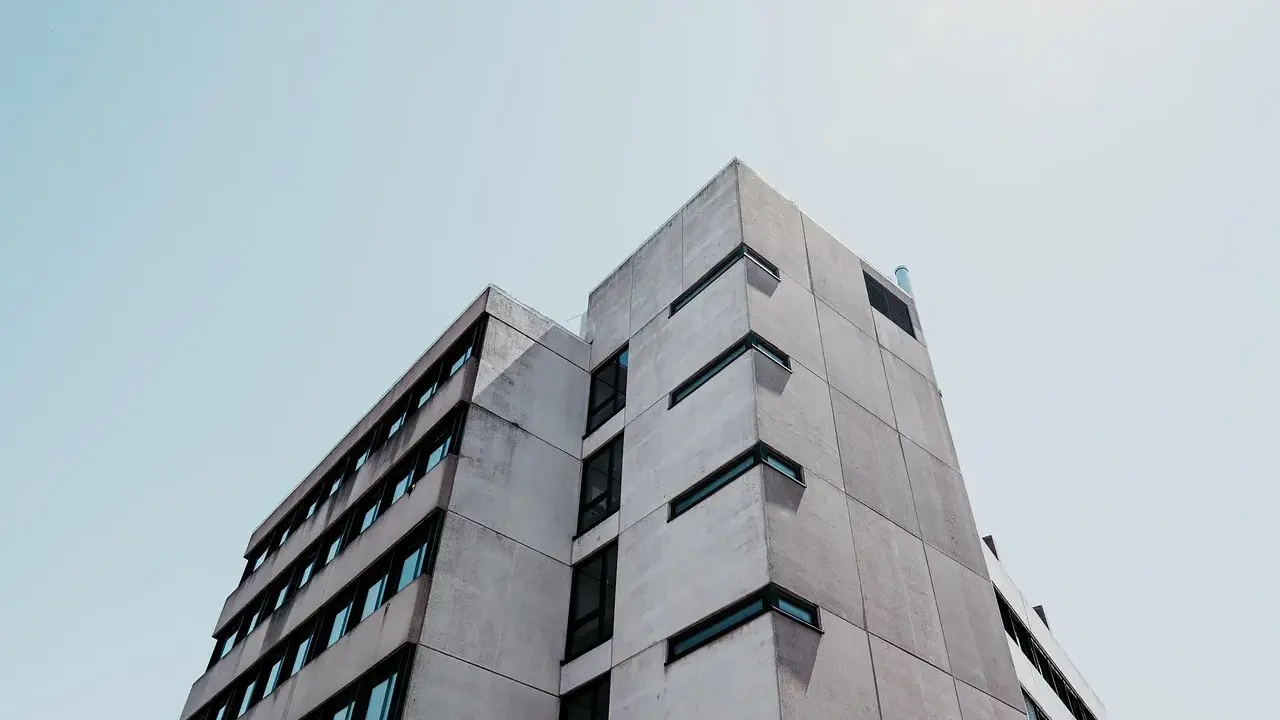 Betonowy budynek o geometrycznej bryle, z rzędami okien. Ta kategoria obiektu budowlanego dominuje w kadrze.