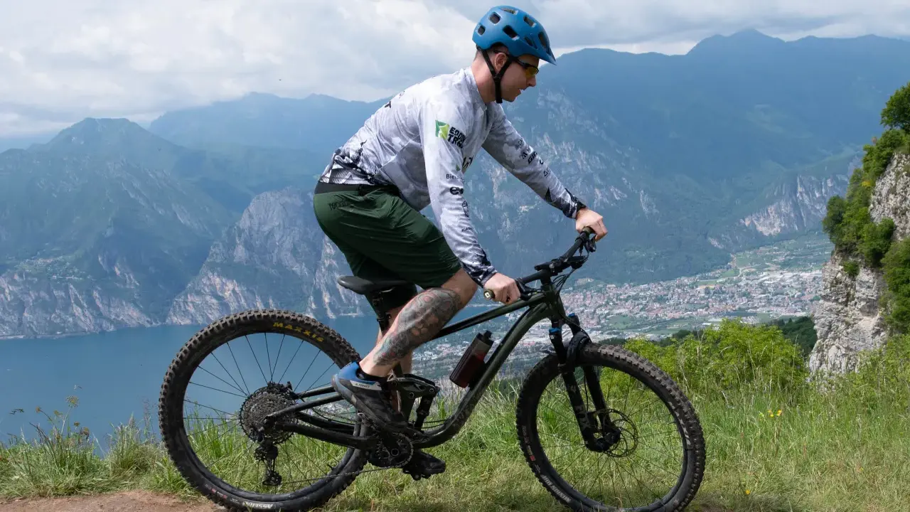 Mężczyzna w kasku jedzie na rowerze MTB po górskim szlaku. Widok na jezioro i miasto w oddali.