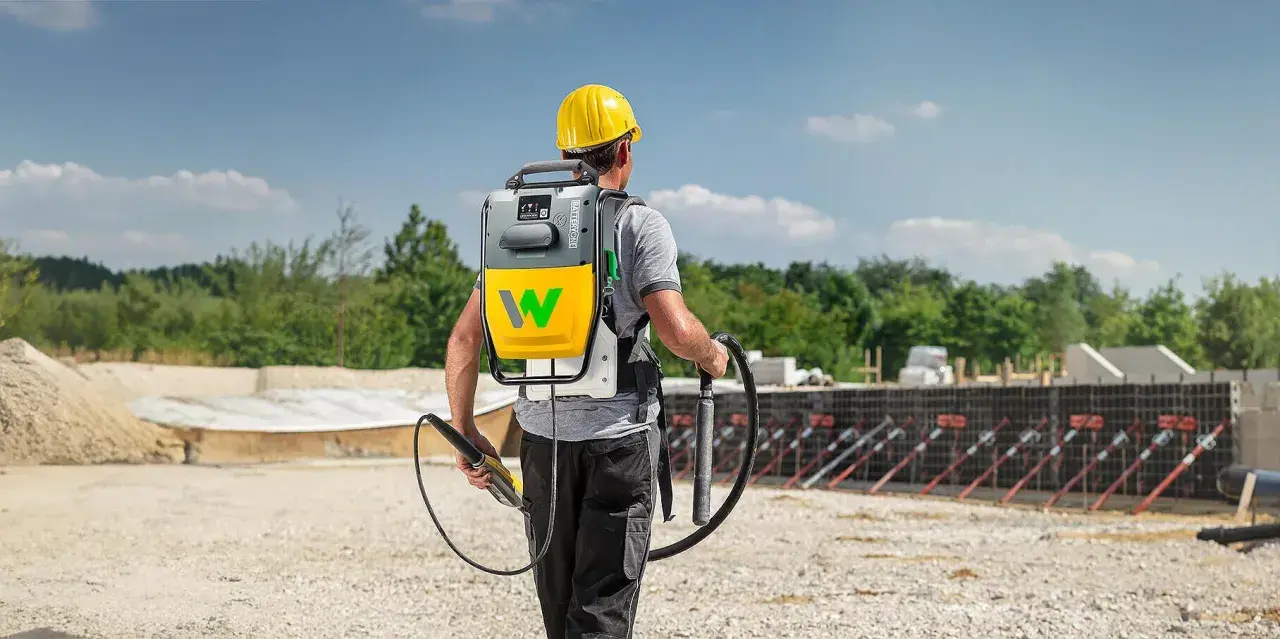 Bauarbeiter mit Rucksackeinheit und Rüttler zur Beton verdichten auf einer Baustelle.