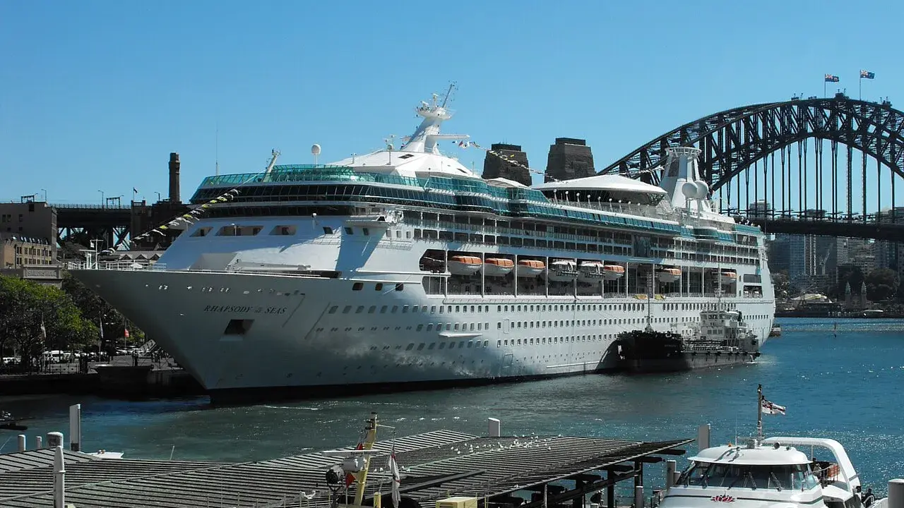 La Rhapsody of the Seas, un'imponente nave da crociera, attracca nel porto di Sydney, con l'iconico ponte sullo sfondo.