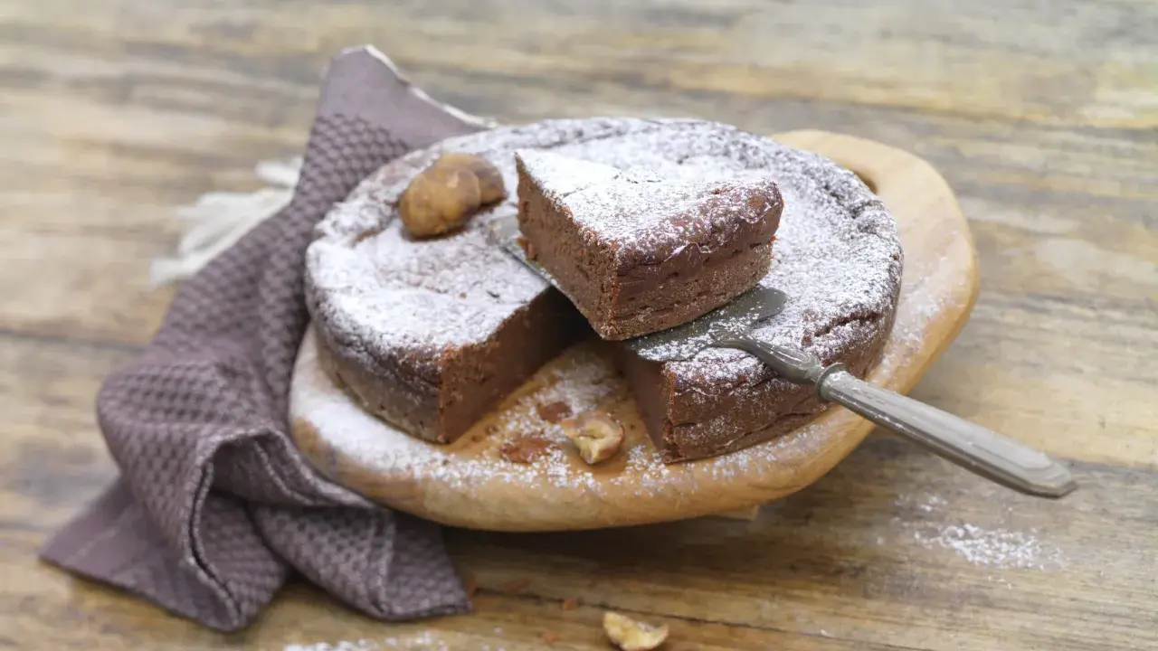 Gâteau au chocolat saupoudré de sucre glace, avec des châtaignes. Une part est coupée, prête à être dégustée. Une recette de châtaigne à essayer !