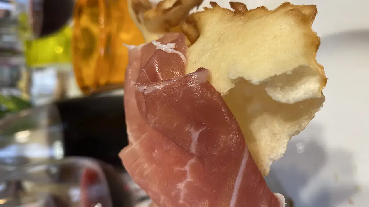 Fetta di gnocco fritto con prosciutto crudo, un classico dei piatti tipici Parma, accompagnato da vino rosso.