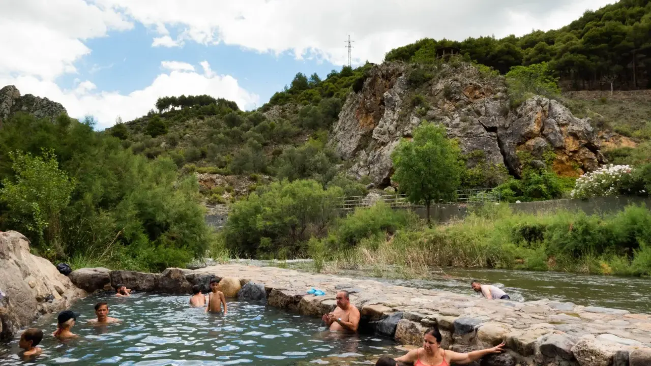 Gente disfrutando de las piscinas naturales en La Rioja, rodeadas de vegetación y rocas.