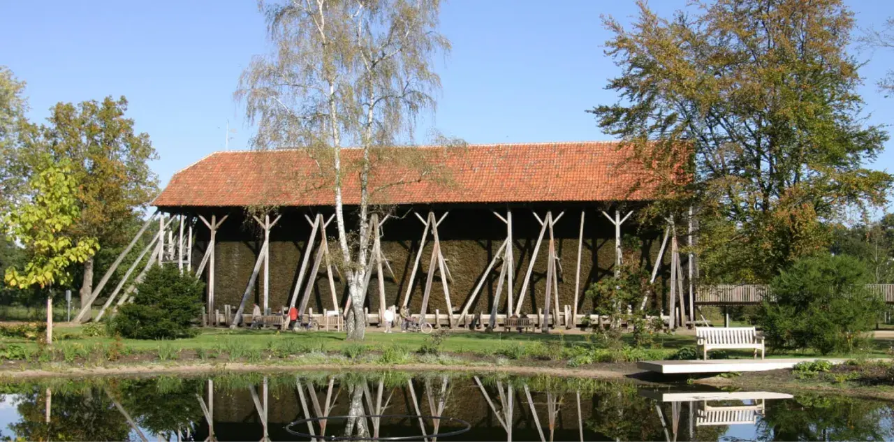 Große Gradierwerke mit roten Ziegeldächern, umgeben von Bäumen und einem Teich. Hier wird die Luft mit gesundem **saline rheine** angereichert.