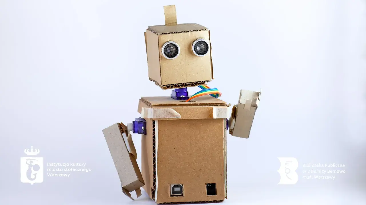 Uroczy robot z kartonu, z oczami-sensorami i kolorowymi kablami, gotowy do nauki i zabawy.