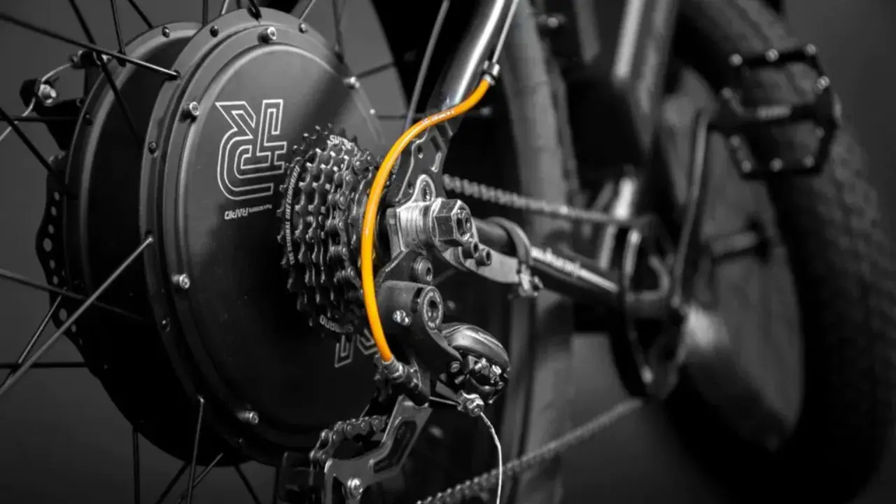 Zestaw do konwersji roweru: czarna piasta z logo, kasetka Shimano, pomarańczowy przewód i przerzutka.