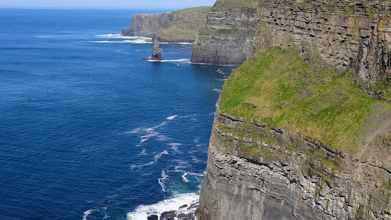 Majestatyczne klify Irlandii wznoszą się nad błękitnym oceanem. Zielone zbocza kontrastują z szarymi skałami, tworząc zapierający dech w piersiach krajobraz.