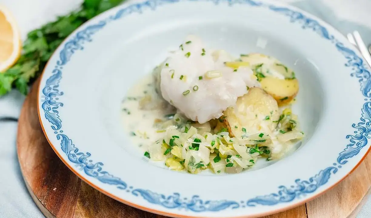 En vacker tallrik med pocherad fisk, potatis och vitkål i en krämig sås, garnerad med gräslök.