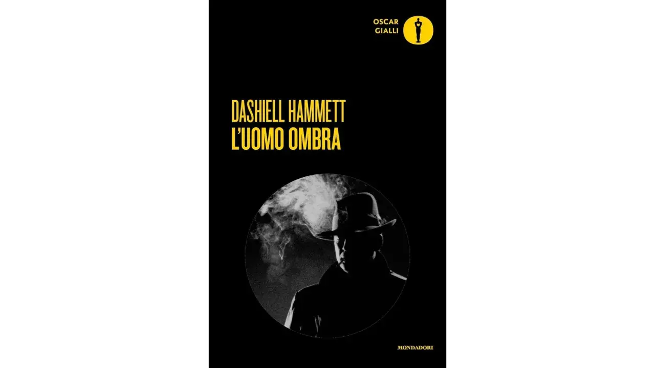 Copertina di "L'uomo ombra" di Dashiell Hammett, un classico dei libri noir. Un investigatore con cappello fuma, immerso nel mistero.