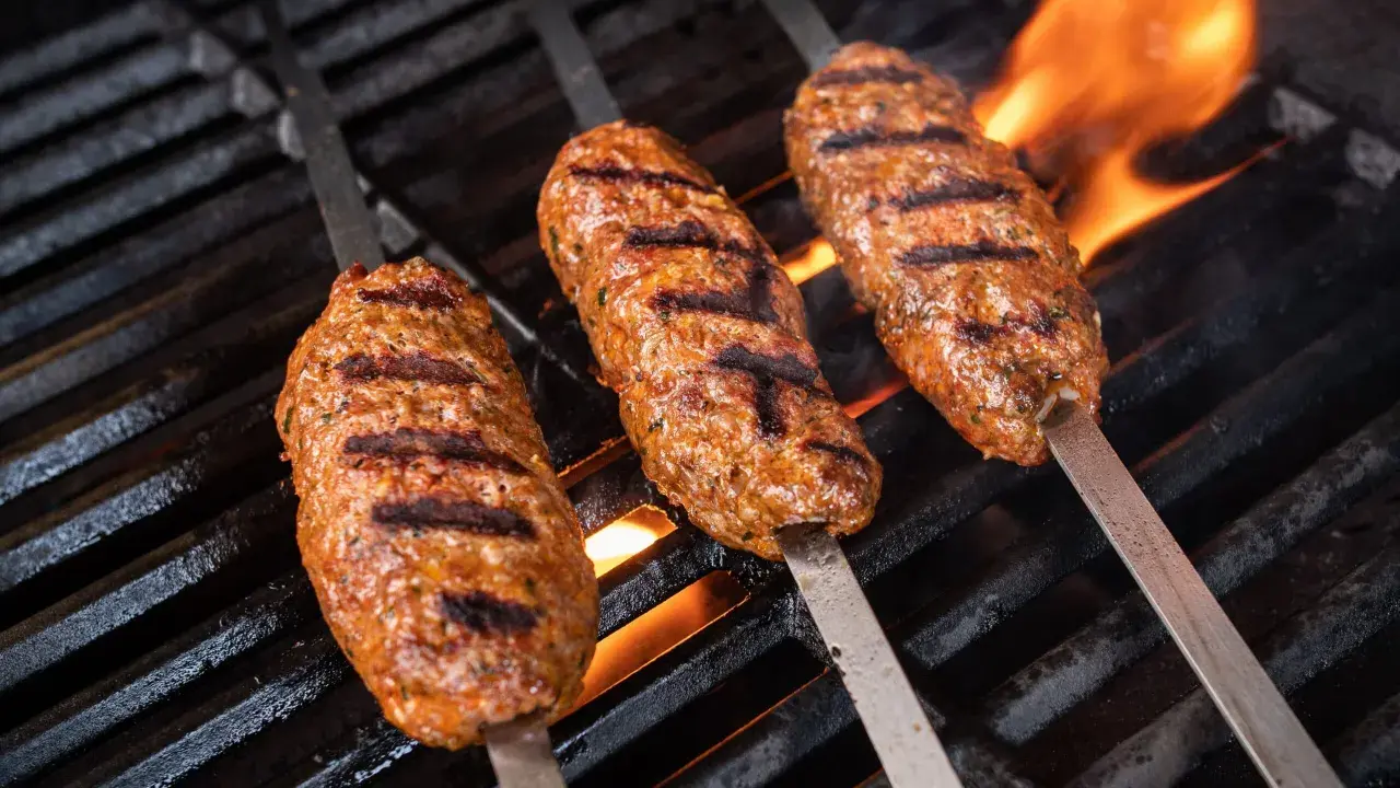 Drei saftige Seekh Kebabs brutzeln auf dem Grill über offenem Feuer.