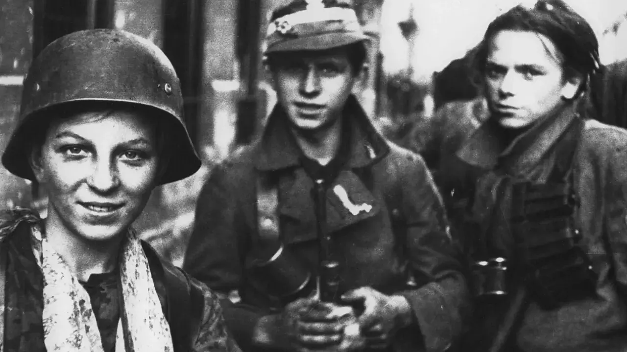 Trzech młodych żołnierzy, być może z Powstania Warszawskiego, w mundurach i hełmach. Jeden z nich uśmiecha się, gotowy do walki.