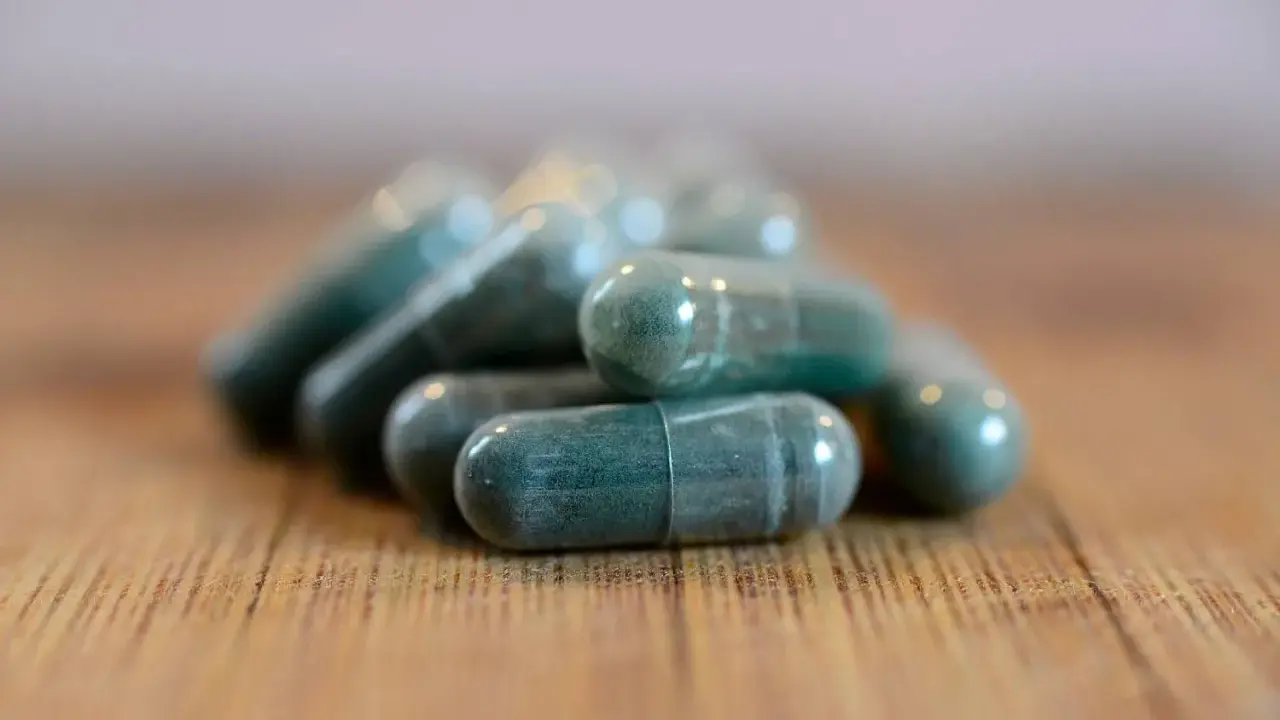 Pile di capsule verdi su un tavolo di legno. Si possono prendere due antibiotici insieme, ma sempre sotto controllo medico.