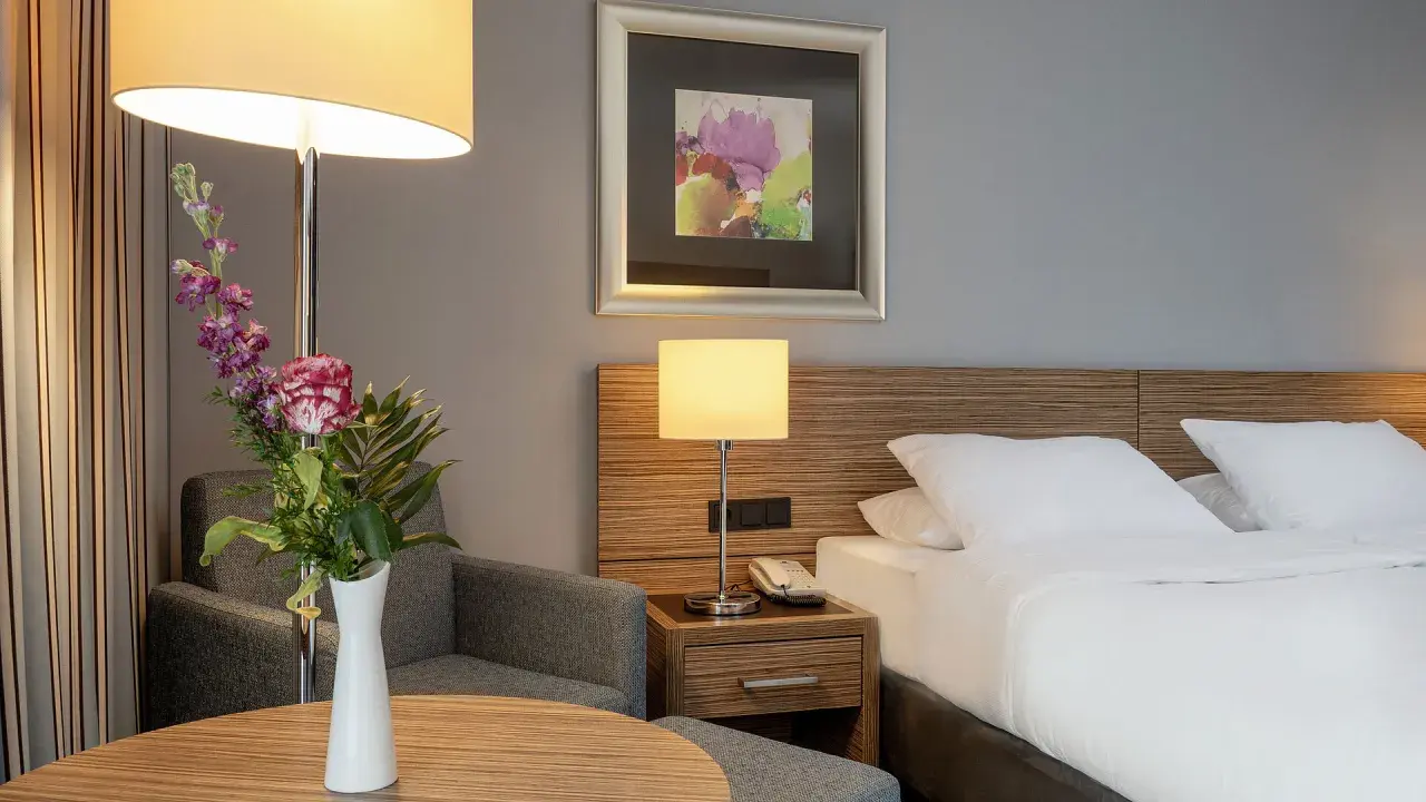 Ein Hotelzimmer mit Bett, Nachttischlampe, Sessel und Blumenstrauß.