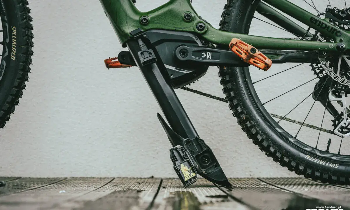 Zielony rower elektryczny z pomarańczowymi pedałami. Widoczny mechanizm, który ułatwia zrozumienie, jak wyjąć baterię z roweru elektrycznego.