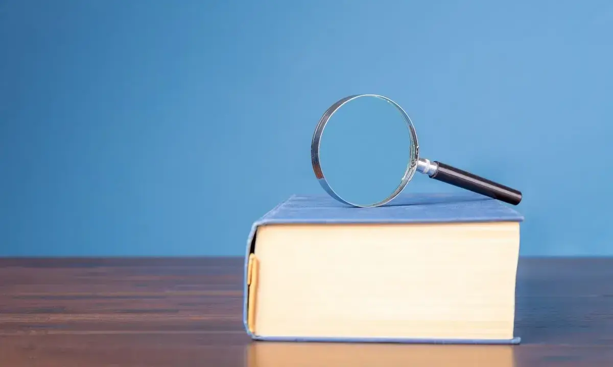 Lente d'ingrandimento su un libro blu, per capire il hic et nunc significato.