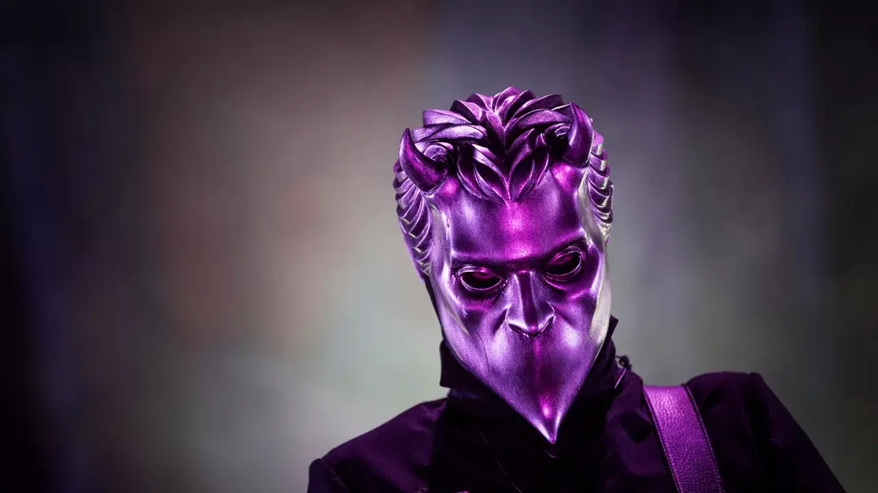 En av Ghost medlemmar utan mask, med en metallisk lila mask som täcker ansiktet.