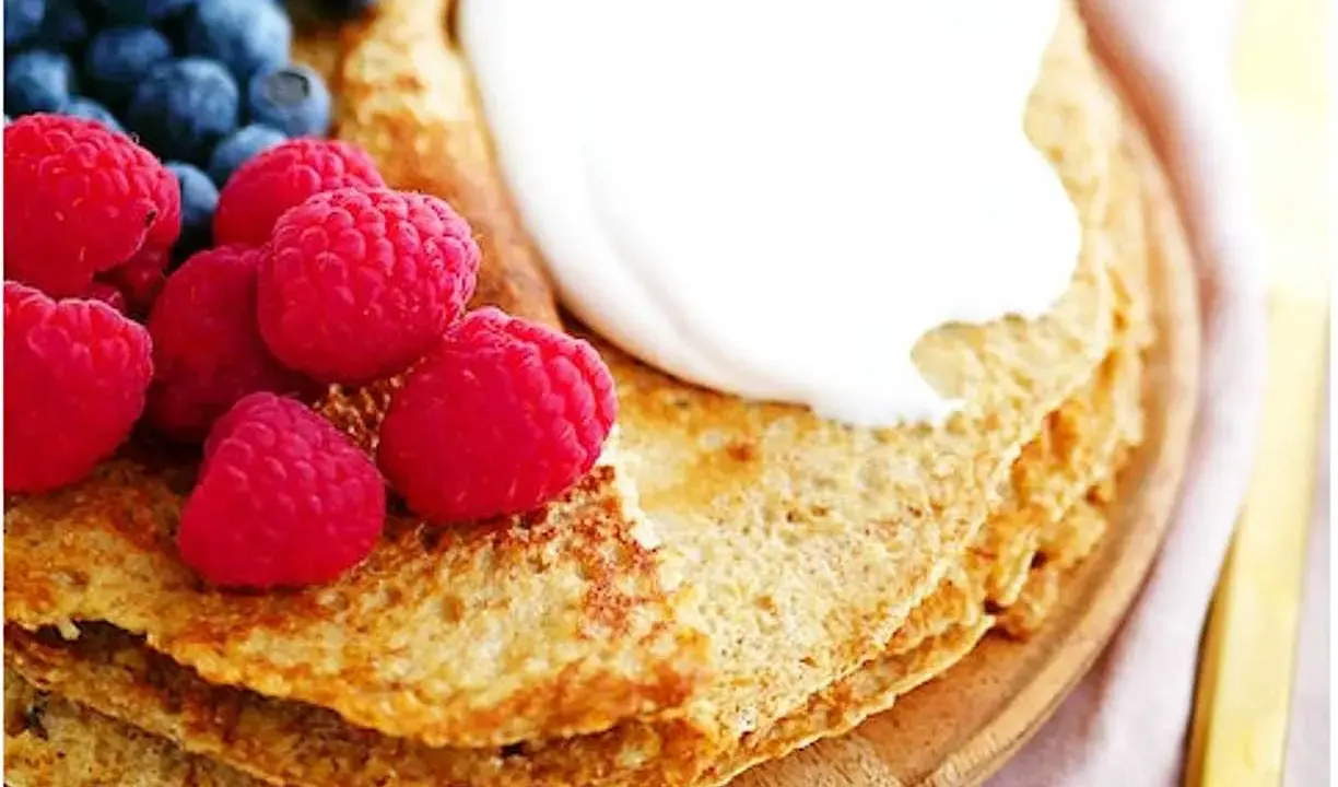 En hög med nyttiga pannkakor toppas med grädde, hallon och blåbär. En perfekt frukost eller mellanmål.