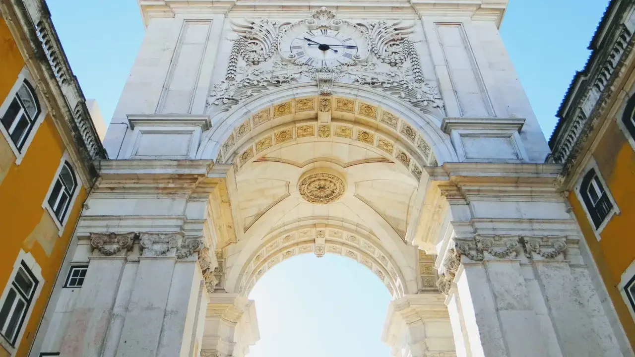 Der Arco da Rua Augusta in Lissabon, ein imposanter Triumphbogen mit einer Uhr und kunstvollen Verzierungen, ragt majestätisch in den blauen Himmel.