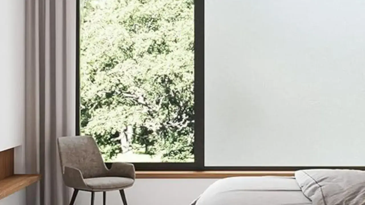 Habitación con cama, sillón y ventana con vidrio mate que filtra la luz del sol y la vegetación exterior.