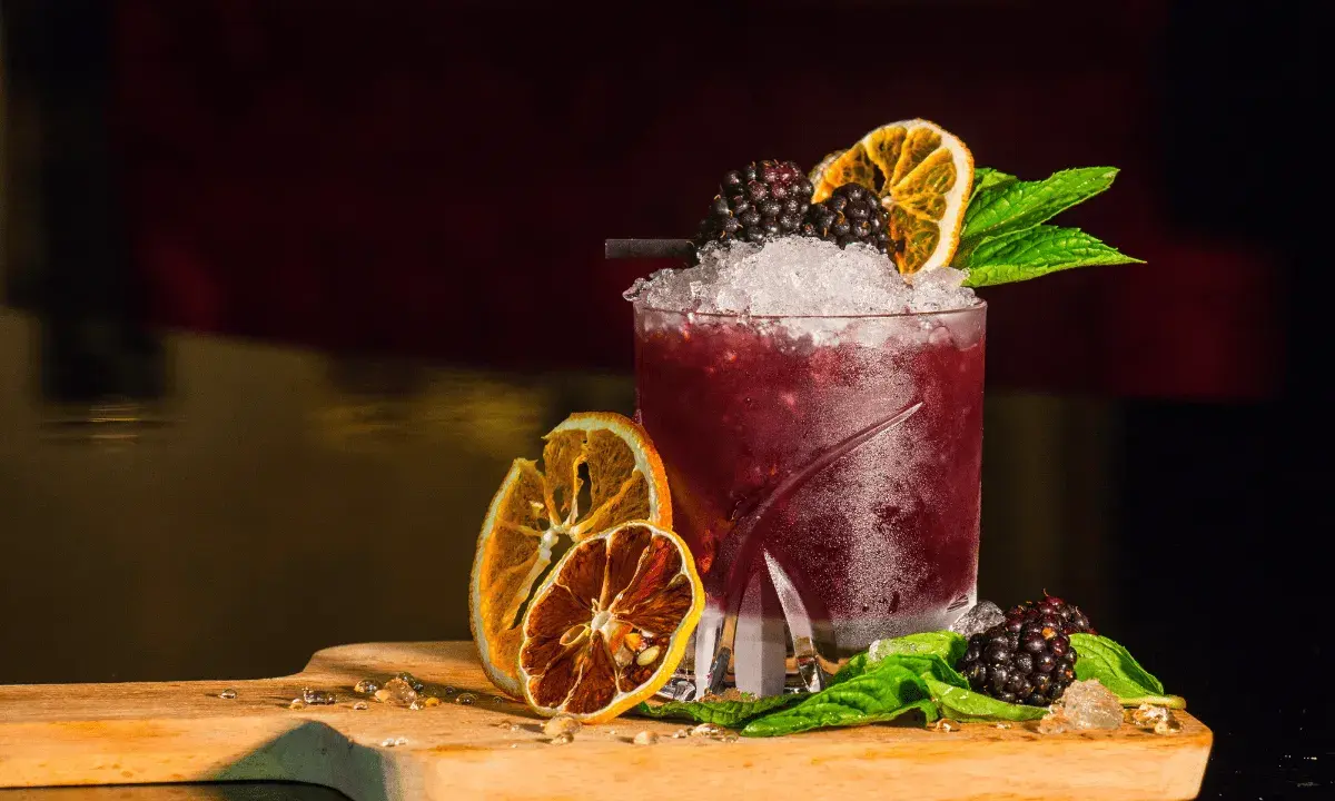 Cocktail rosso con frutti di bosco, arancia essiccata e menta, perfetto per un aperitivo a Riccione.