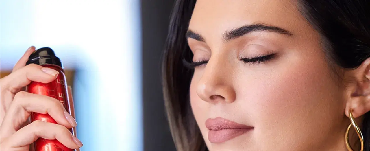 Una mano sostiene un spray fijador de maquillaje rojo. Ideal para cuando usar y mantener tu look perfecto.