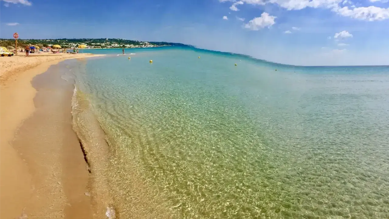 Spiaggia delle Maldive in Puglia: sabbia dorata, acque cristalline e un cielo azzurro con nuvole bianche. Un paradiso terrestre.
