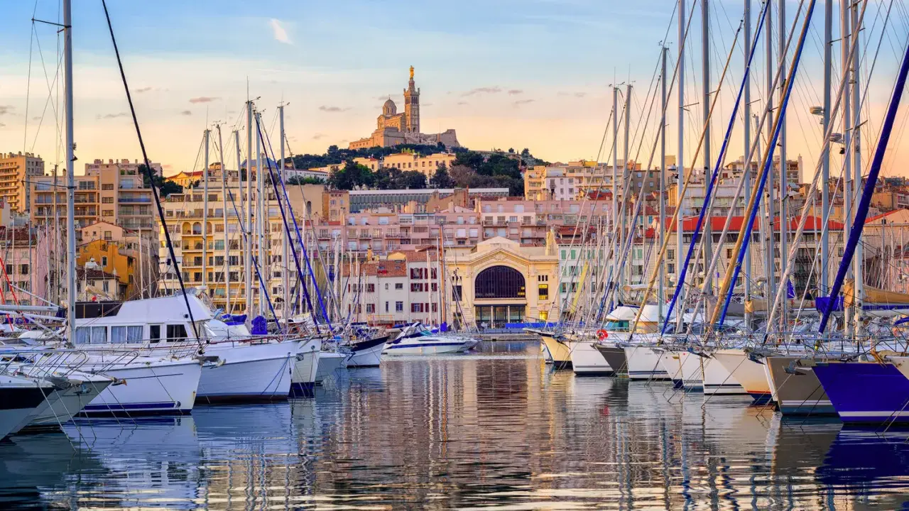 Barche a vela ormeggiate nel porto di Marsiglia, con la Basilica di Notre-Dame de la Garde sullo sfondo. Un'ottima vista per chi cerca cosa vedere a Marsiglia vicino al porto.
