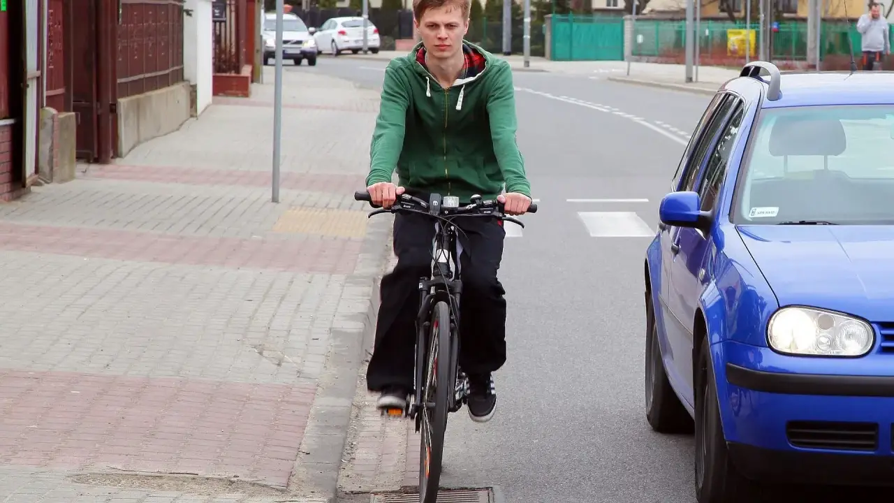 Młody mężczyzna na rowerze jedzie po chodniku, obok drogi. To miejsce, gdzie można jeździć bez karty rowerowej.