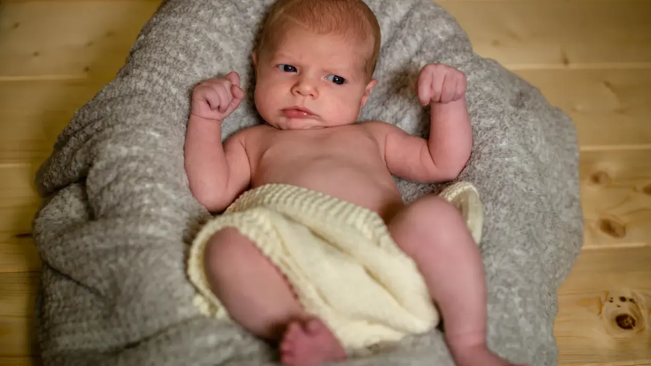 Un neonato con un'espressione curiosa, avvolto in una coperta, pronto per un servizio fotografico flash neonati.