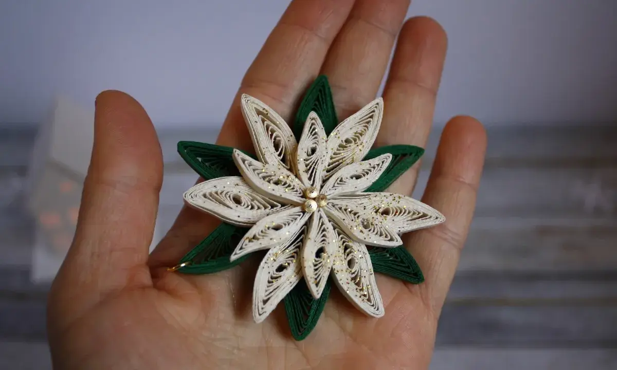 Un fiore di carta in quilling, perfetto per un tutorial di quilling natale. Dettagli dorati e petali bianchi e verdi.