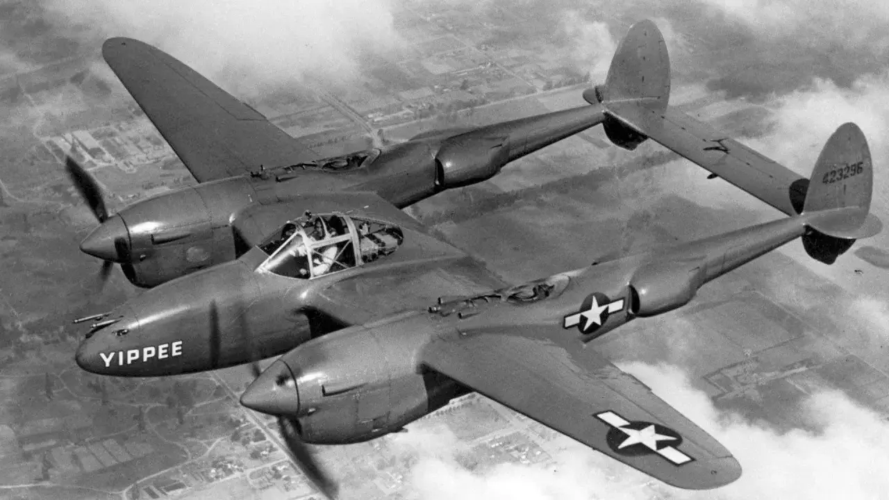 Ein P-38 Flugzeug mit dem Namen "YIPPEE" fliegt über Wolken.