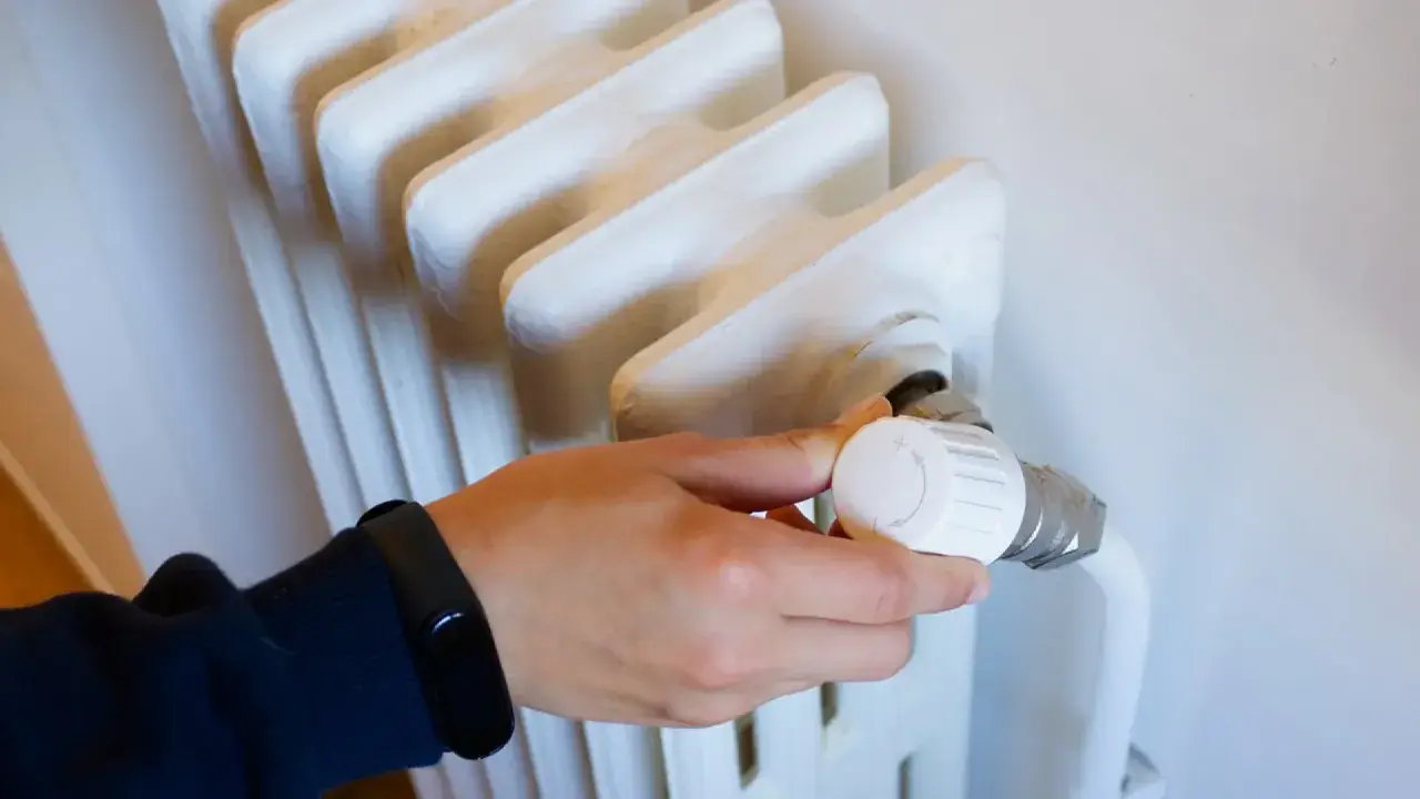 Mano ajustando el termostato de un radiador blanco. Controlar la temperatura ayuda a saber cuanto cuesta la calefaccion al mes.