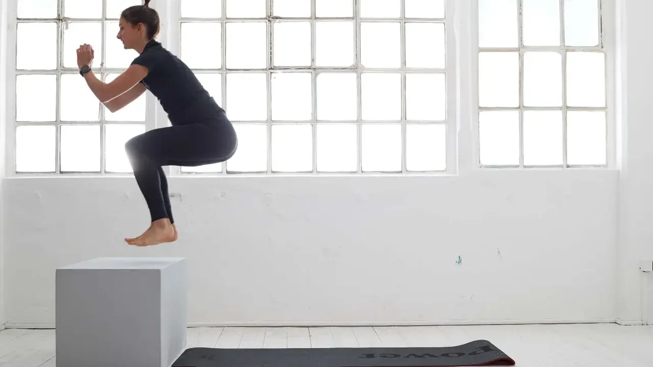 Frau macht **box jumps** in einem hellen Raum mit großen Fenstern.