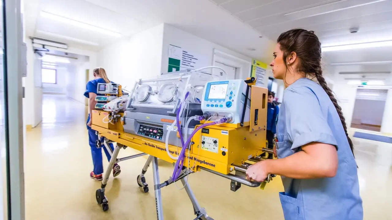 Infermiera spinge un'incubatrice mobile in un corridoio ospedaliero. Quanto tempo in terapia intensiva neonatale è cruciale per questi piccoli pazienti.